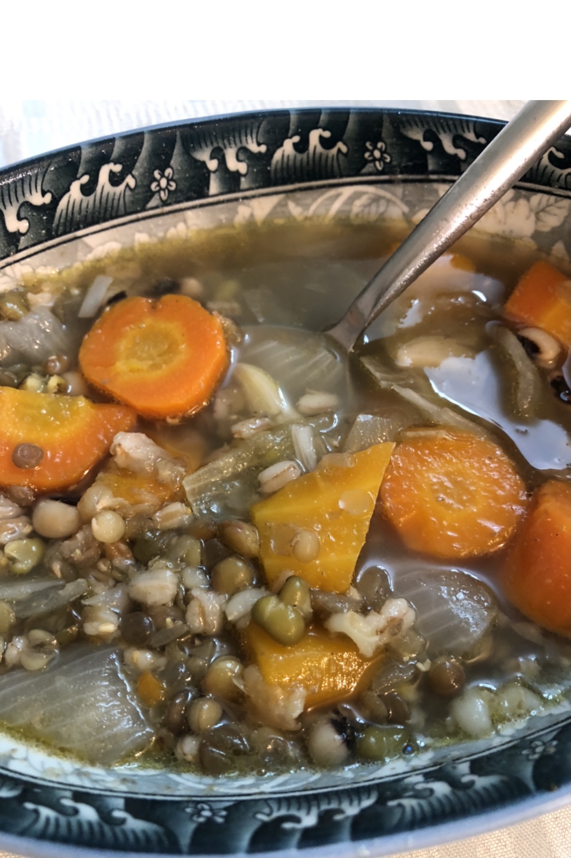 Ceramic bowl of vegetable soup with barley, spelt, legumes, carrots, celery and onions.