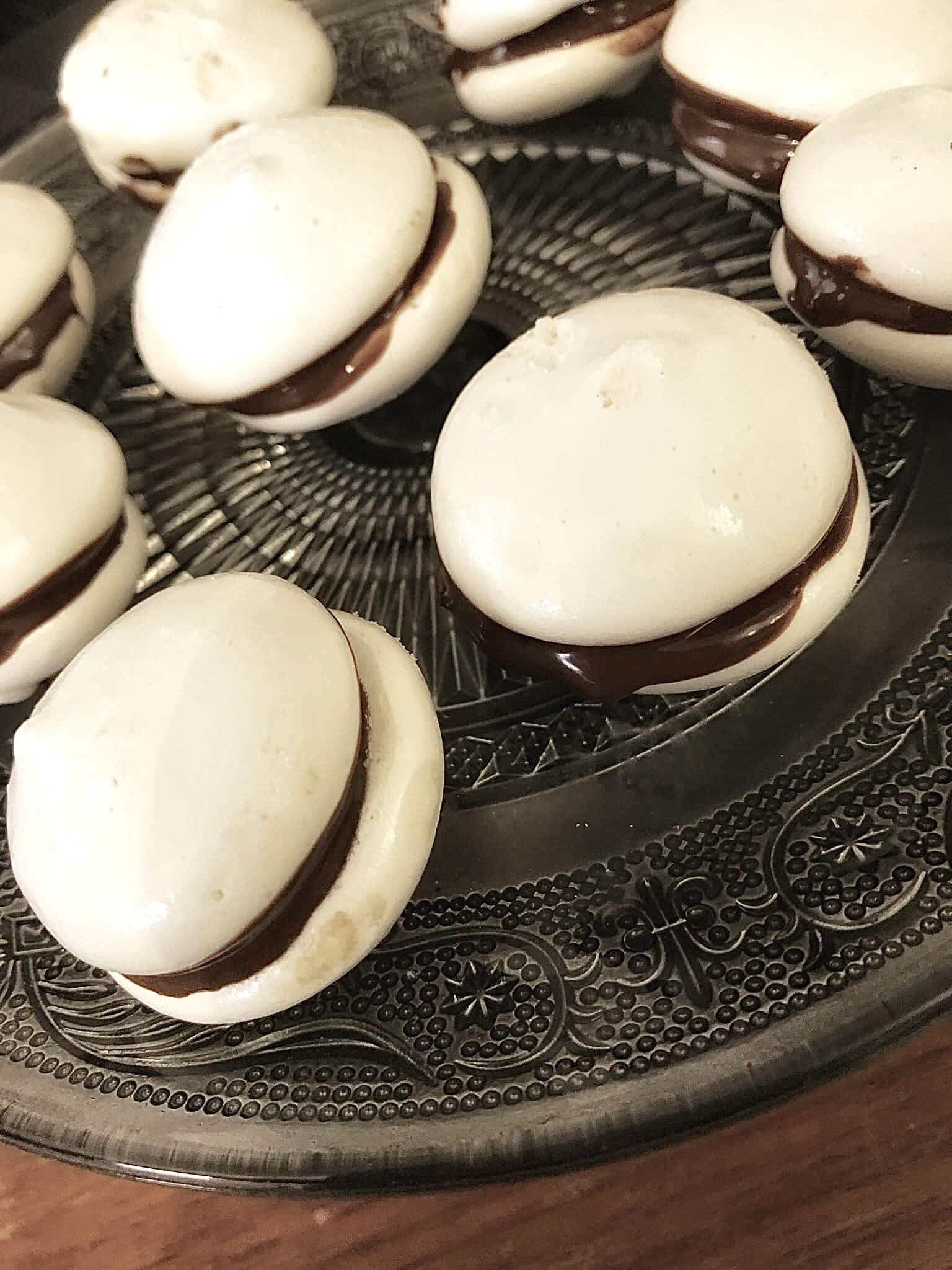 Meringues sandwiched with chocolate in between on a glass platter